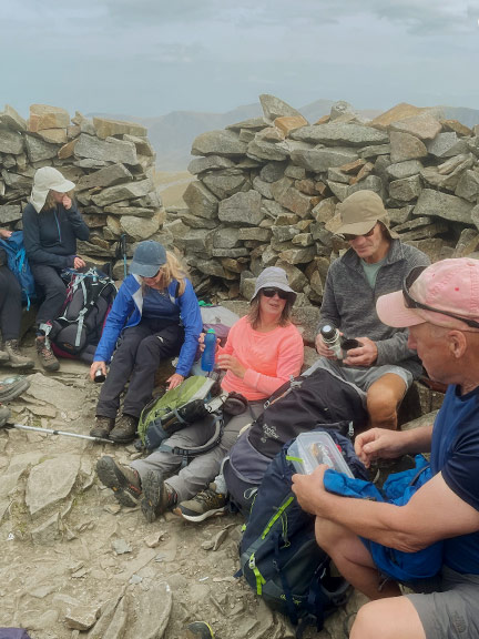 4. Pedol Marchlyn Horseshoe
26/04/26. Lunchtime in the refuge cairn at the summit of Elidir Fawr. The right half of the group. Photo: Noel Davey.
Keywords: Apr26 Sunday Gareth Hughes
